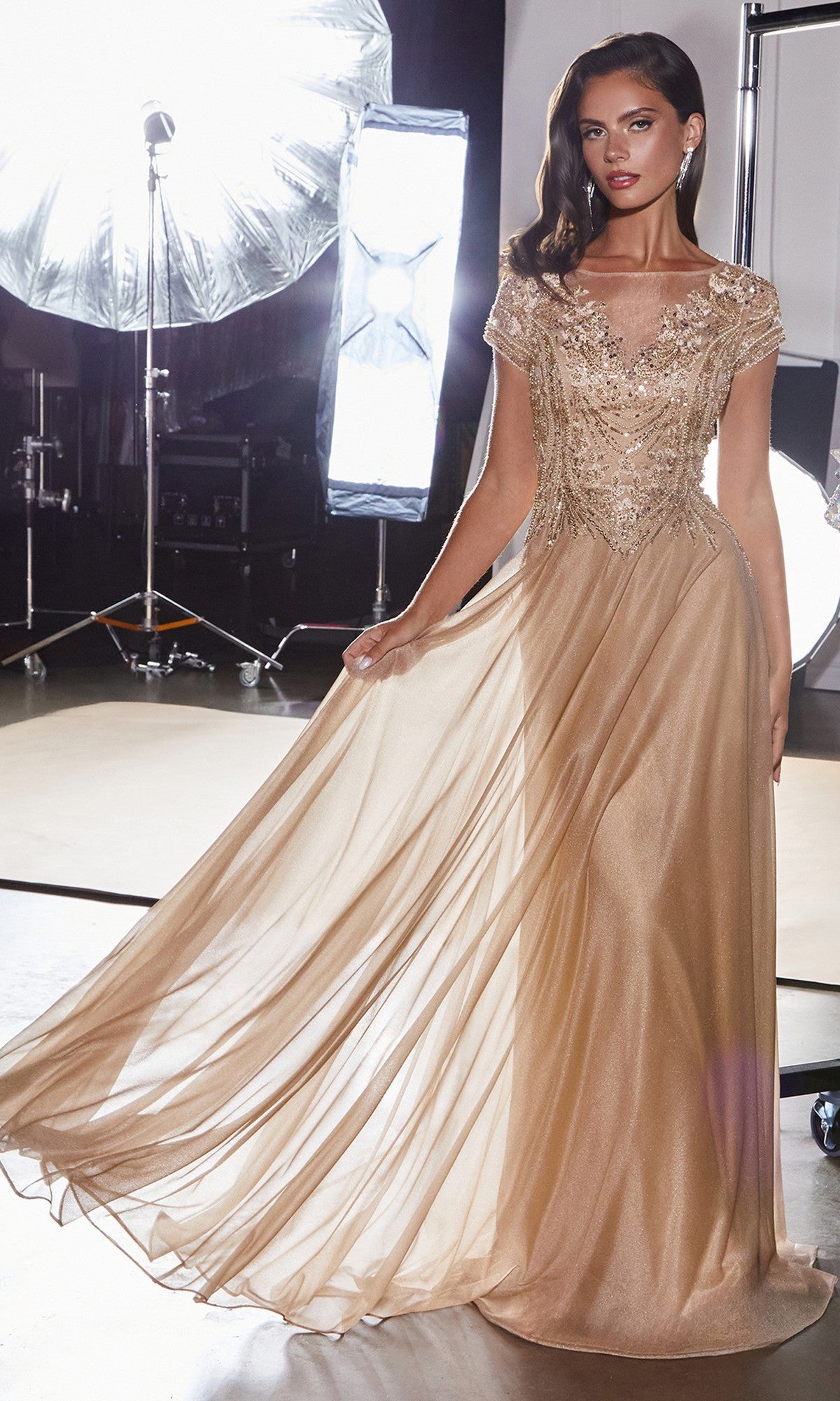 A woman wearing the Ladivine CL11 Long Formal Dress with a beaded bodice poses in a photography studio, bright lights and equipment in the background.